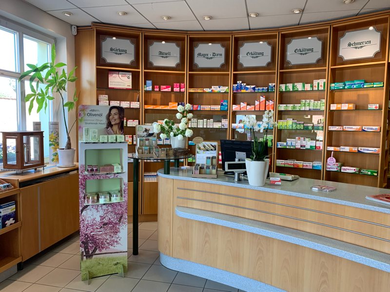 Innenansicht der Mauritius-Apotheke in Jüterbog mit geschwungener Holz-Offizin, zahlreichen Regalen voller Arzneimittel, dekorativen Pflanzen und eine